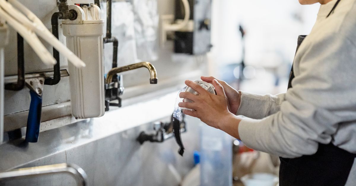 A person processes film in a darkroom with visible plumbing and equipment, showcasing the art of traditional photography.